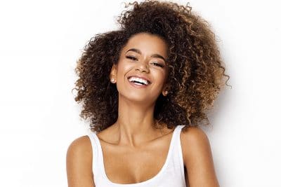 Young woman with big, curly hair shows off her big, bright smile